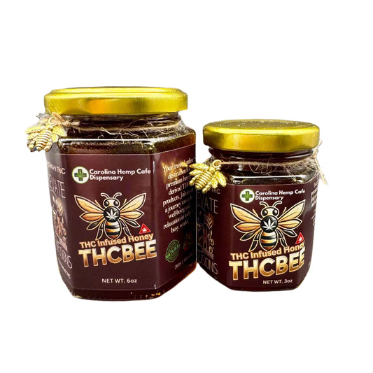 Two jars of THCBee THC honey on a wooden surface, one jar is larger than the other, both have a yellow lid and a label with the brand name and bee imagery.