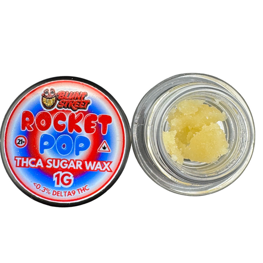 A round clear jar of Blunt Street Rocket Pop THCA Sugar Wax 1G shown next to its red, blue, and white label lid, with pale yellow wax crystals visible inside the open jar.