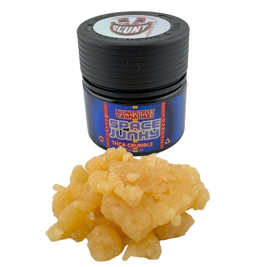 Jar of 'Space Junky' cannabis product with a small amount of crumble on a white background