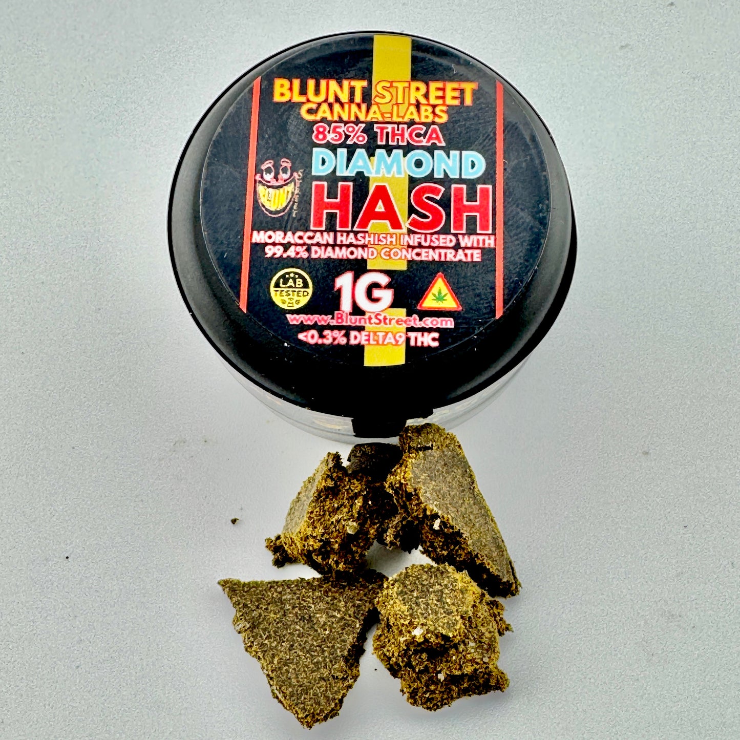 Container of Blunt Street Cannatabs Diamond Hash with cannabis buds on a gray background