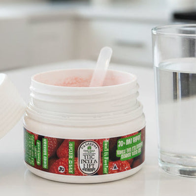 An open white jar of Calypso Rosemary Hair Growth Balm with a clear plastic spatula inside, next to its matching white lid on a dark gray surface.