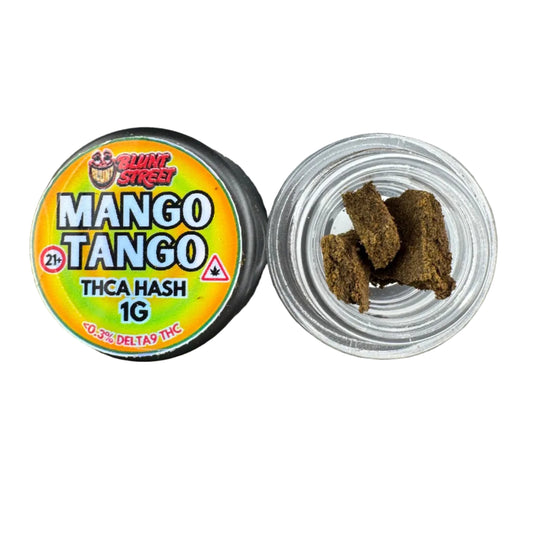 A 10g jar of Mango Tango Trica Hash 1G fishing hook bait by The Hook Gang, shown with its lid off to reveal several dark brown hash pieces inside a clear plastic cup, set against a dark gray textured background.