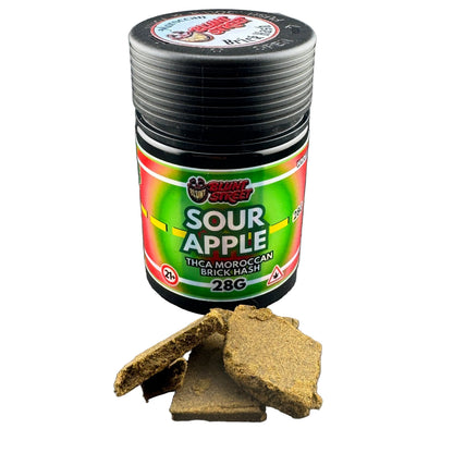 A jar of Sour Apple brand Moroccan brick hash with a black lid and a green, red, and yellow label, shown on a dark gray background with pieces of the brown hash in front.
