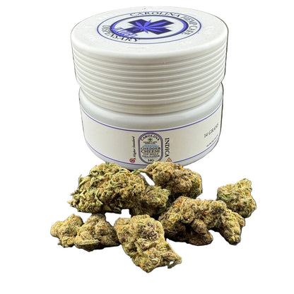 A white plastic jar labeled 'Carbogen Remedies Triphop' with several green and brown dried flower buds placed in front of it on a dark gray surface.