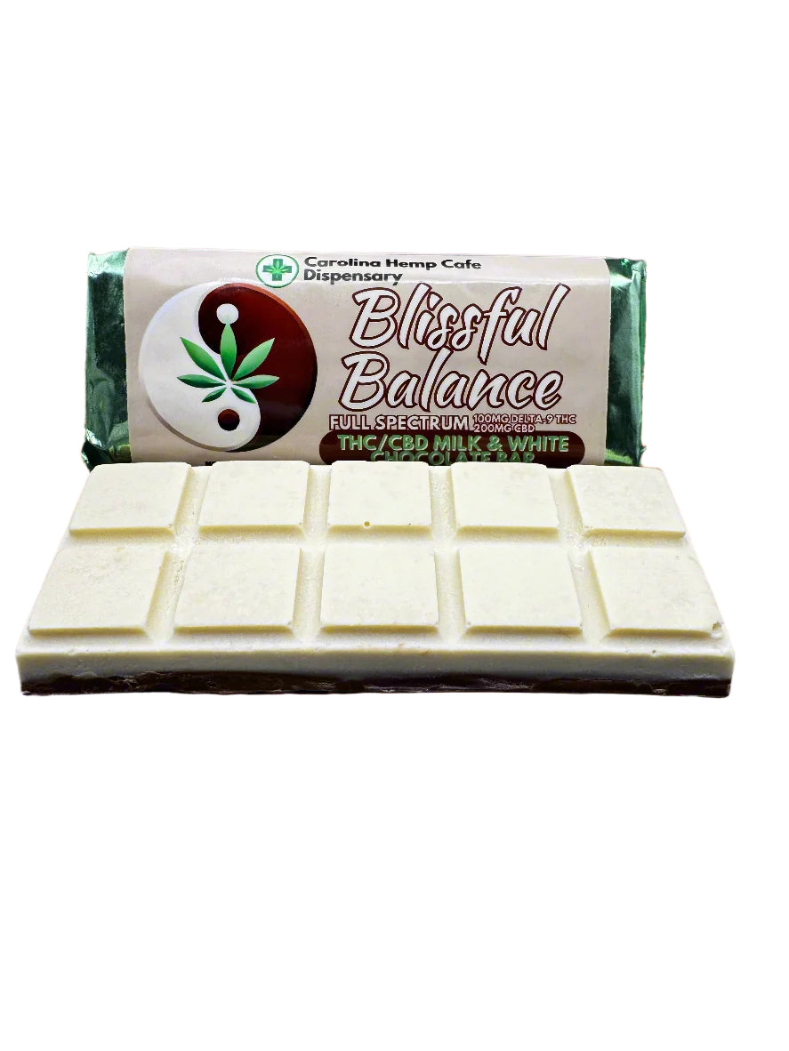 A chocolate bar with a split into milk and white chocolate pieces, branded as 'Blissful Balance' with a cannabis leaf logo, set against a backdrop of a sunset with silhouetted people in the distance.
