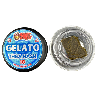 A round blue and black container labeled 'BLUNT STREET GELATO THCA HASH 1G' shown next to an open clear plastic jar containing a square piece of dark green-brown hash oil.