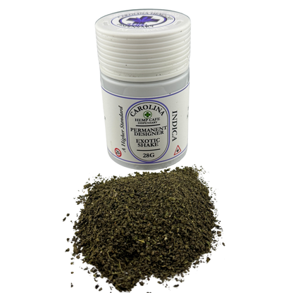 A small white plastic jar labeled Carolina Hemp Cafe Permanent Designer Exotic Shatter Indica 28G, shown with a pile of dark green ground flower in front on a white background.